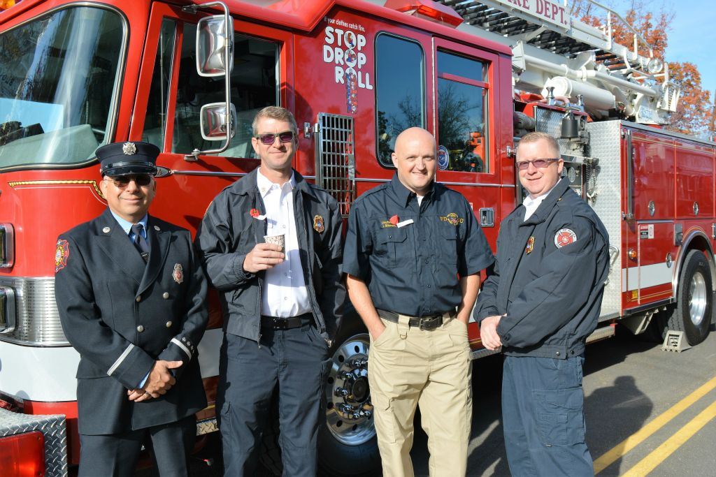Four members of the Fire Department stand beside the firetruck, looking into camera and smiling